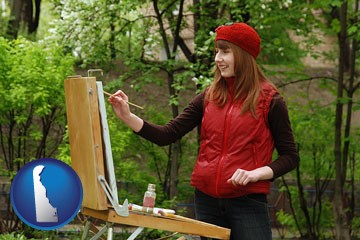 a female plein air artist painting with oils on a portable easel - with Delaware icon