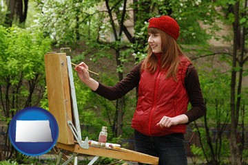 a female plein air artist painting with oils on a portable easel - with North Dakota icon