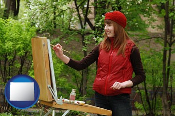a female plein air artist painting with oils on a portable easel - with Wyoming icon